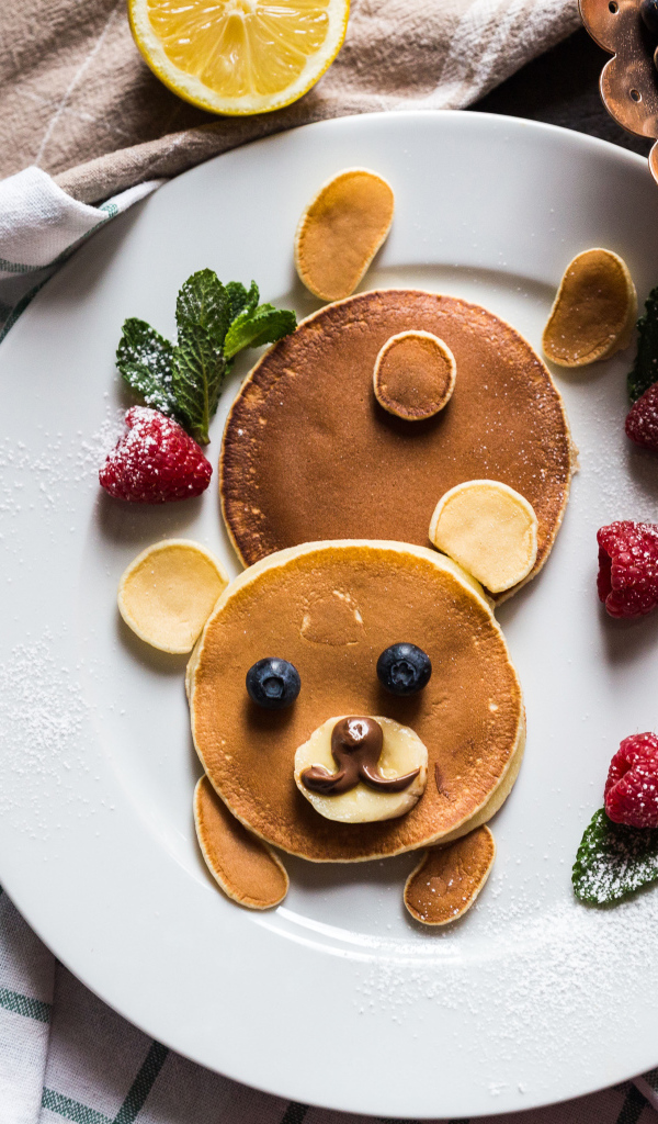 Медведь из оладьев на тарелке с малиной и сахарной пудрой