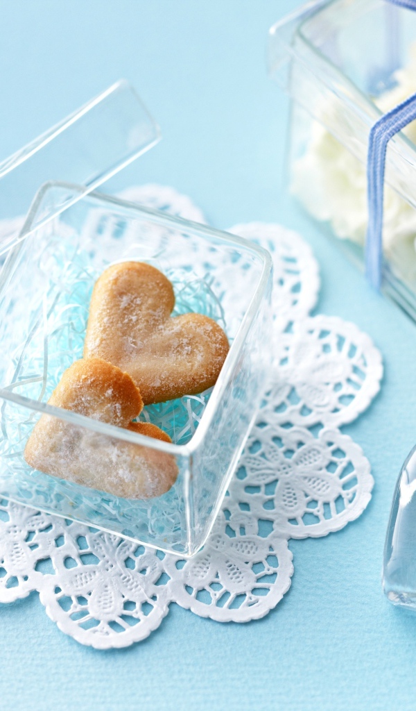 Песочное печенье в форме сердца в стеклянной шкатулке на голубом столе 