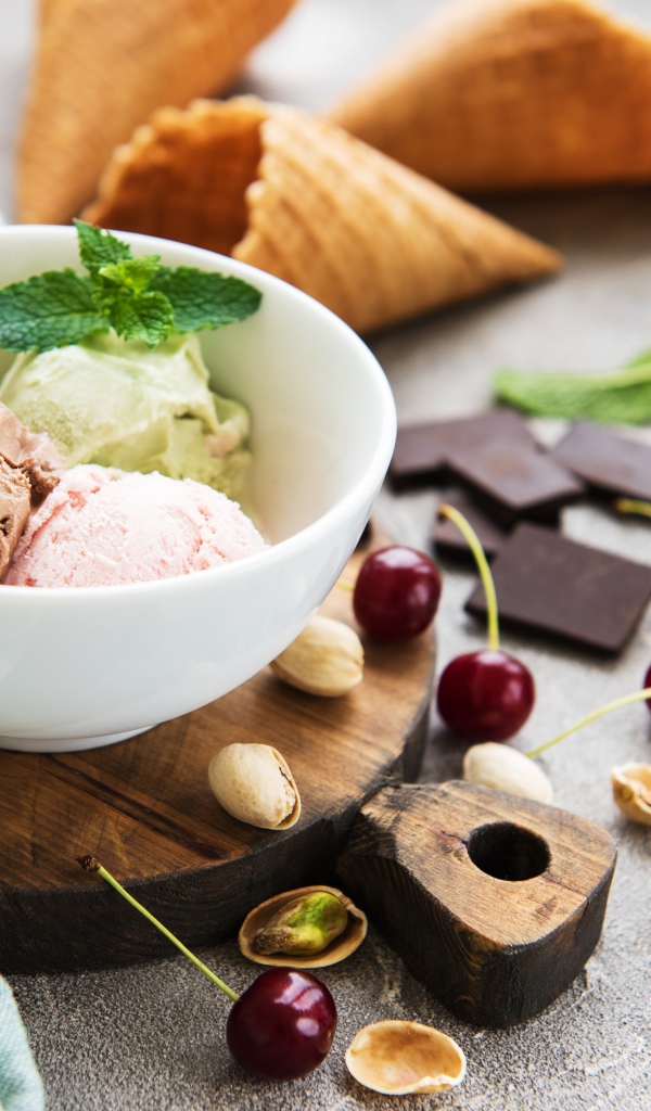 Шарики мороженого на столе вафельными рожками, черешней и фисташками