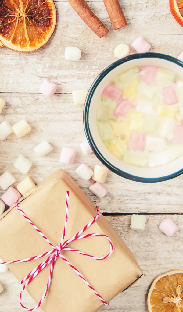 Кружка горячего напитка на столе с маршмеллоу, пряностями и подарком