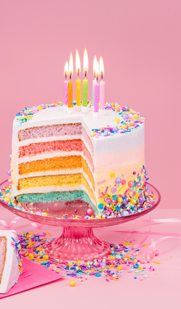Разноцветный праздничный торт со свечами на розовом фоне