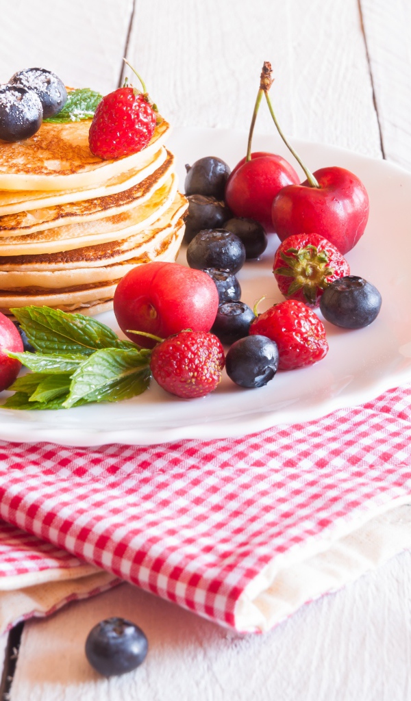 Оладья на белой тарелке с ягодами черники, черешни и клубники