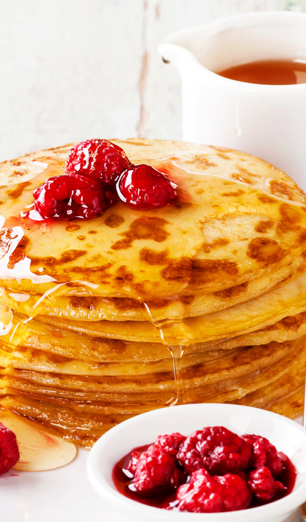 Панкейки с медом и ягодами малины на столе с чаем