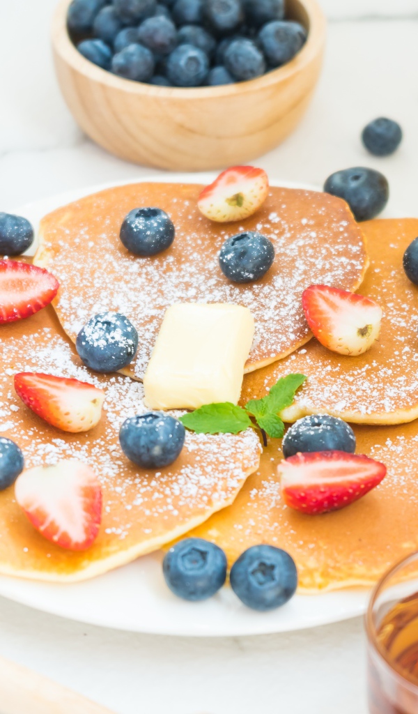 Оладьи с сахарной пудрой, клубникой и черникой на столе