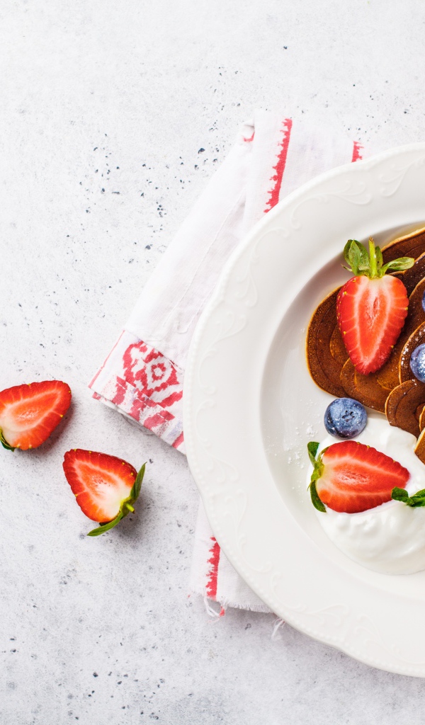 Оладьи со сметаной в тарелке с ягодами черники, клубники и красной смородины