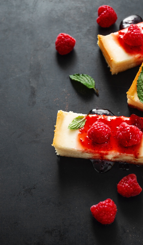 Куски чизкейка на столе с джемом и ягодами малины