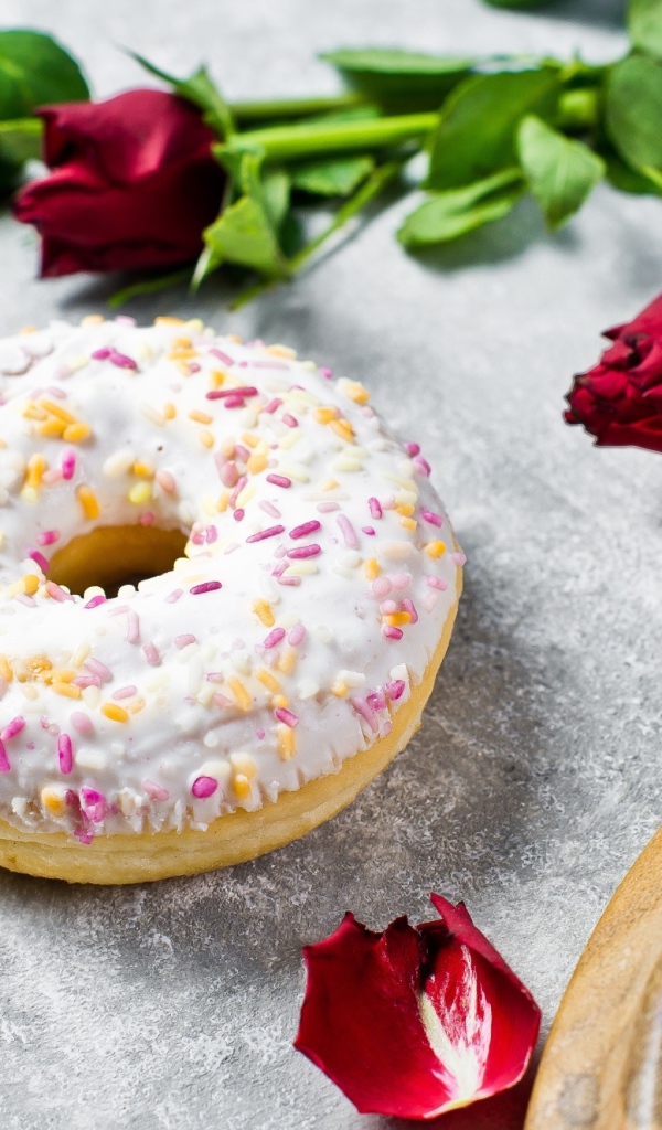 Сладкий пончик с глазурью на столе с красными розами