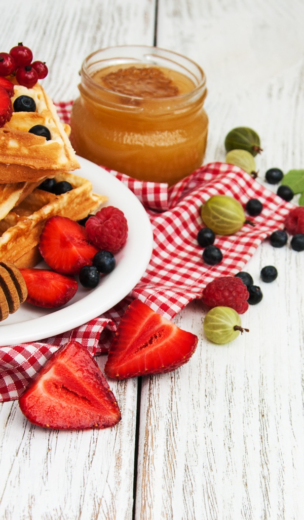 Сладкие вафли на столе с ягодами и медом