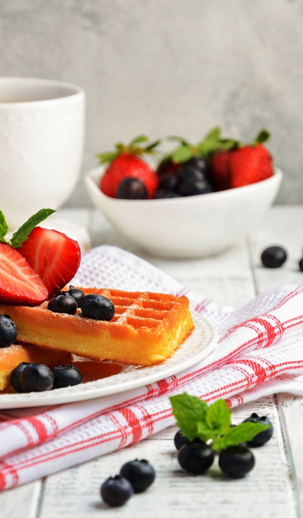 Сладкие вафли с ягодами черники и клубники на столе с медом и чаем