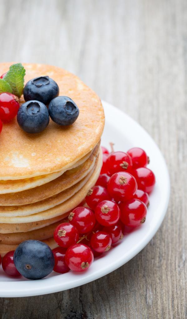 Вкусные оладьи на тарелке с ягодами красной смородины и черники