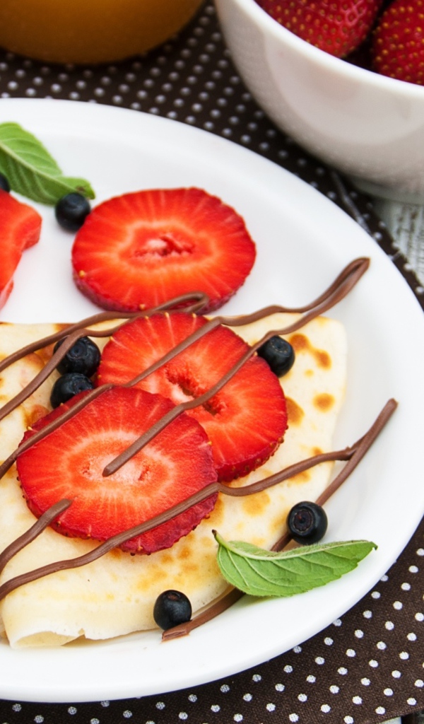 Тонкий блинчик на тарелке с шоколадом, ягодами клубники и черники