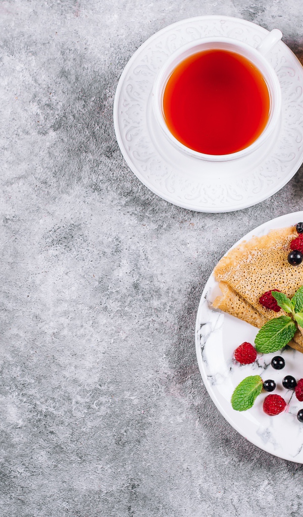 Тонкие блинчики на столе с ягодами, чаем и медом