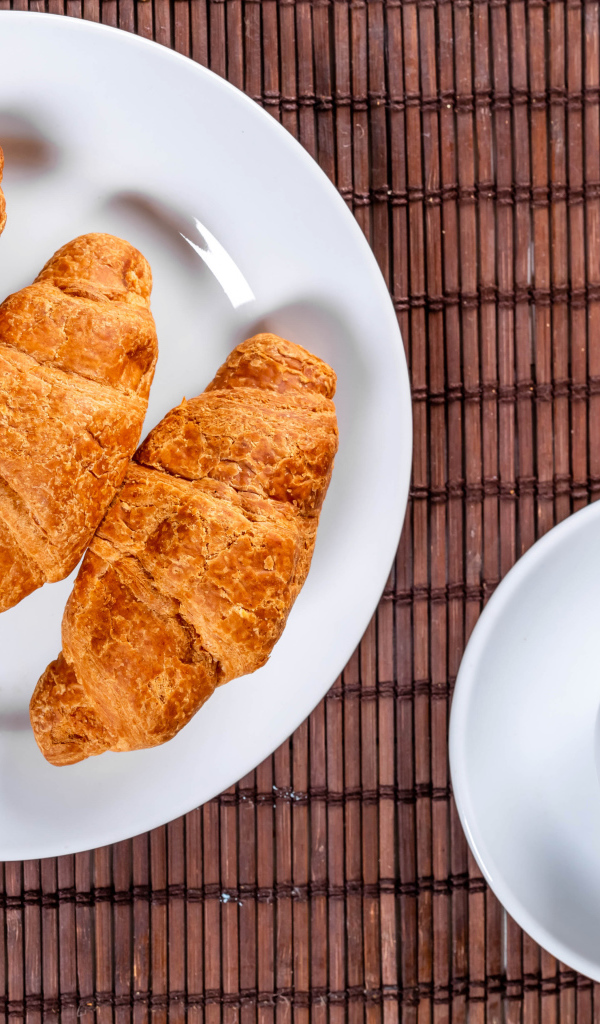 Три круассана на белой тарелке на столе с чаем