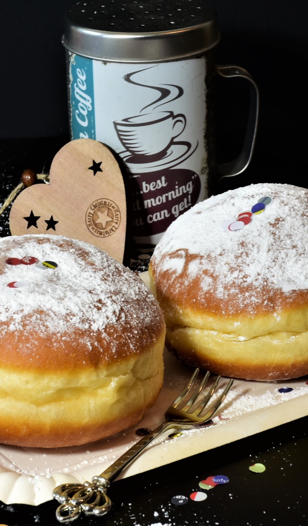 Два пышных пончика с сахарной пудрой на черном столе с кофе