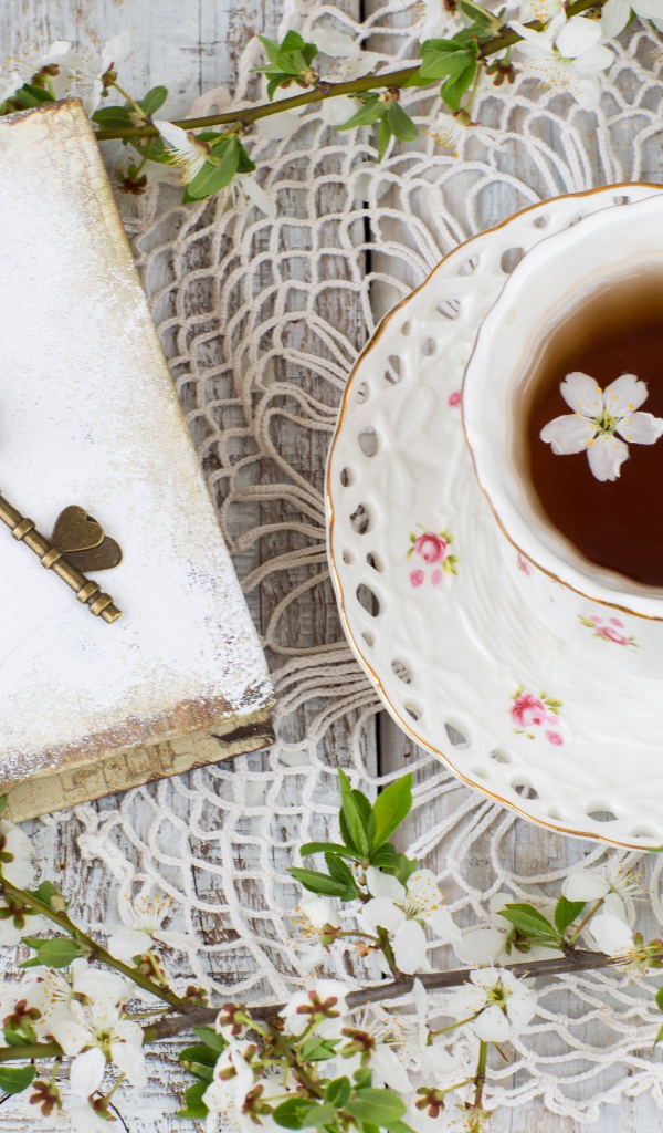 Чашка чая на столе с книгой и белыми цветами вишни 