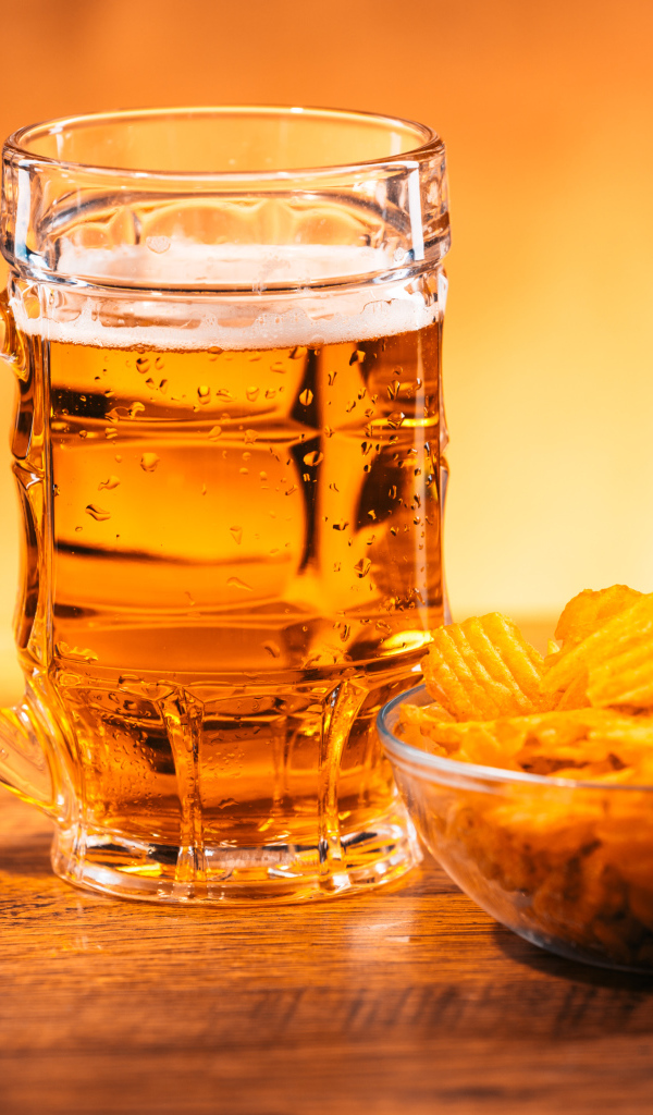 Бокал пива с тарелкой чипсов на столе 