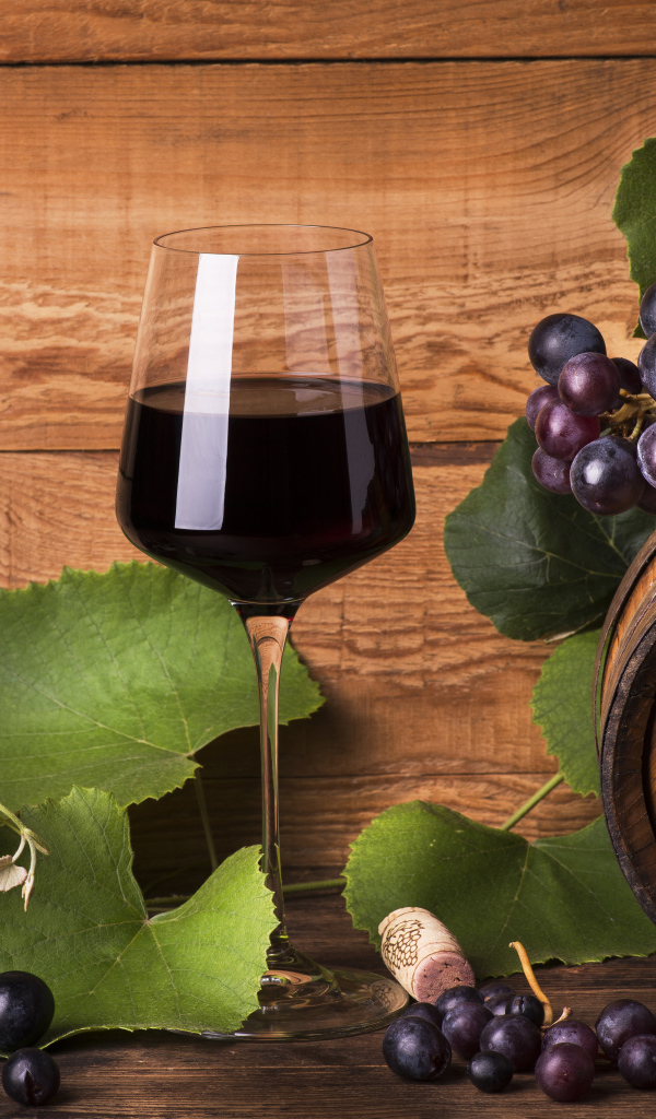 Бокал красного вина  на столе с виноградом и бочкой