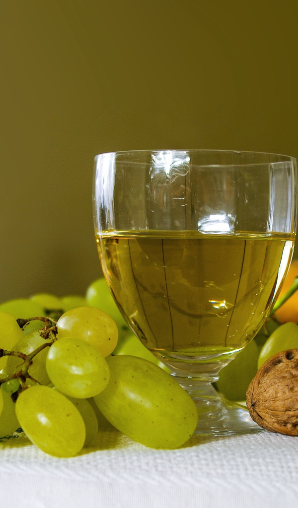 Бокал белого вина на столе с виноградом и орехами