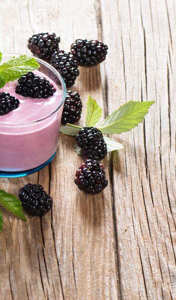 Стакан йогурта на деревянном столе с ягодами ежевики