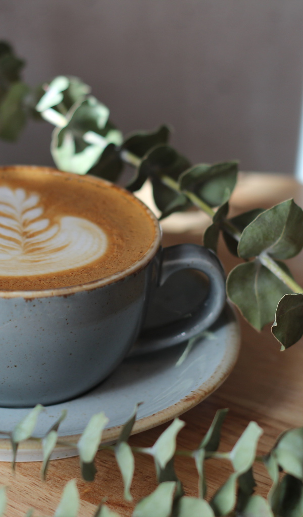 Большая чашка кофе с рисунком на пене на столе с веткой