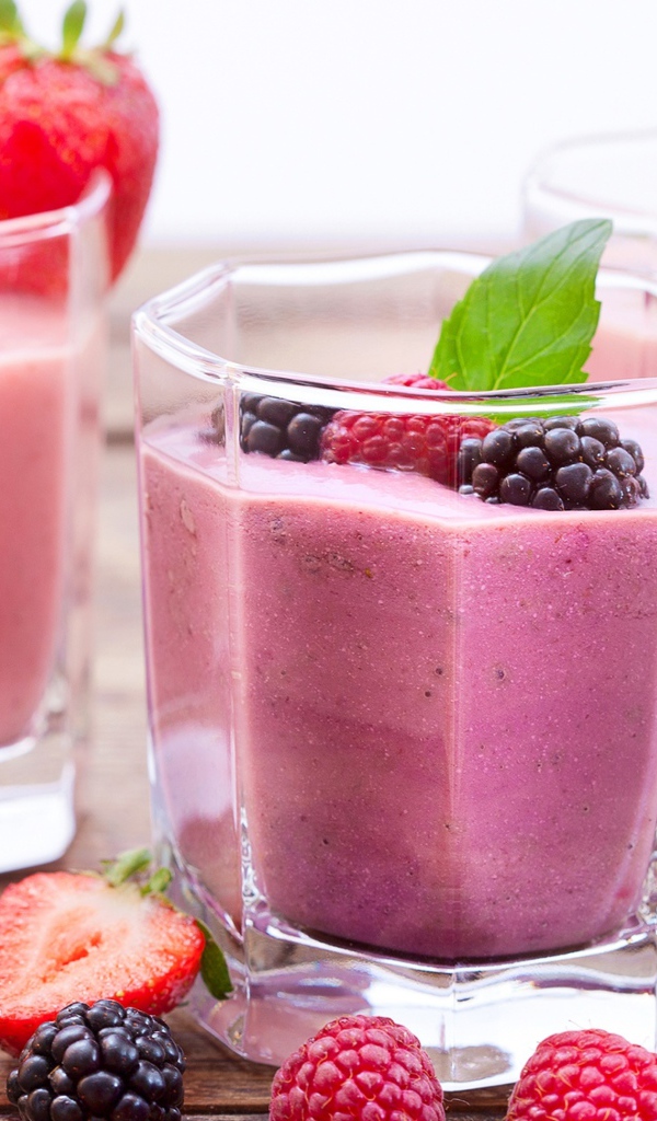 Ягодное смузи в стаканах на столе с ягодами малины, черники и клубники