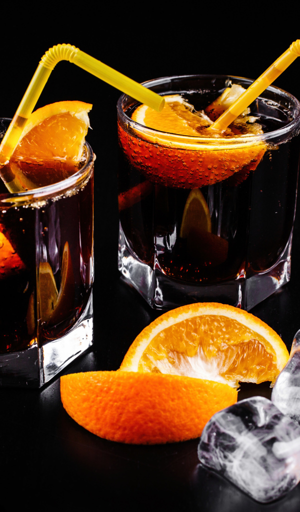 Коктейль с кусочками апельсина на черном фоне со льдом