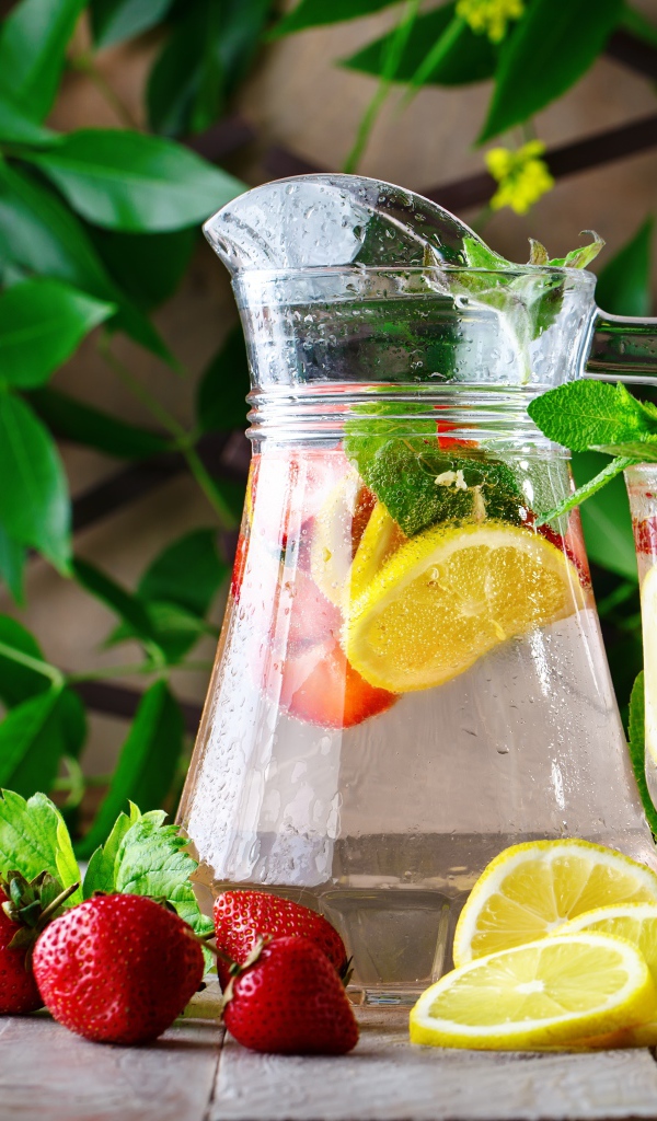 Холодный мохито в графине на столе с клубникой и лимоном