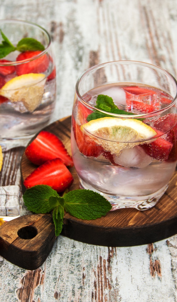 Холодный мохито на столе с ягодами клубники, лимоном и мятой