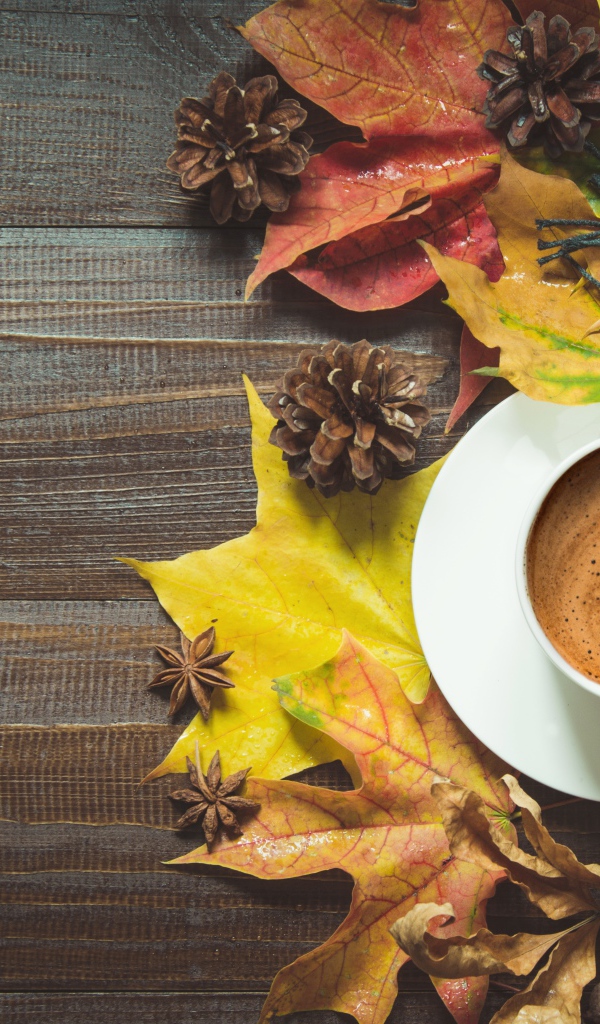 Чашка кофе на столе с шарфом, желтыми листьями и шишками