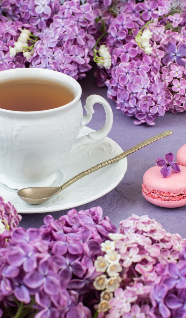 Чашка чая на столе с цветами сирени и десертом макарон
