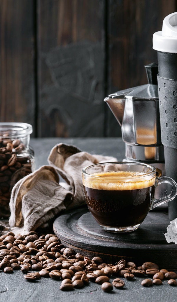 Стеклянная чашка кофе на столе с термосом и зернами