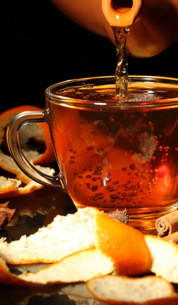 Стеклянная чашка с чаем на столе с апельсинами и корицей