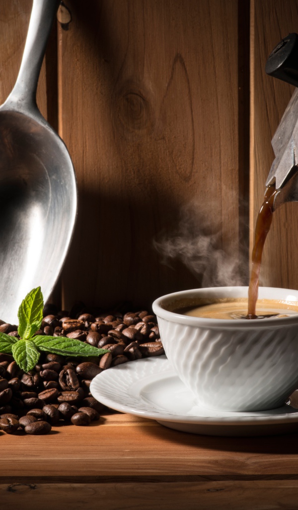 Горячий кофе наливают в белую чашку на столе с кофейными зернами