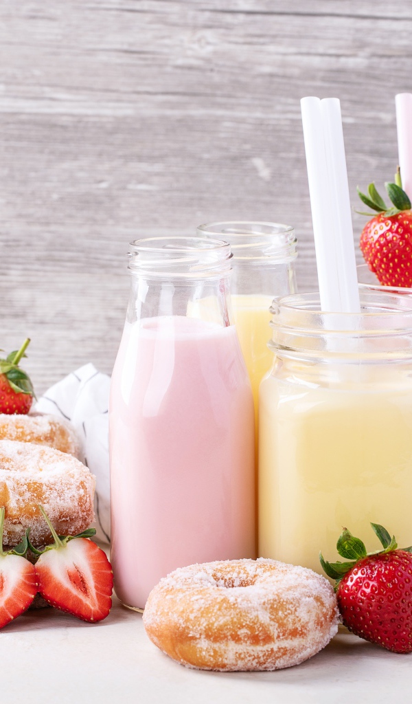 Молочные коктейли на столе с пончиками и ягодами клубники 