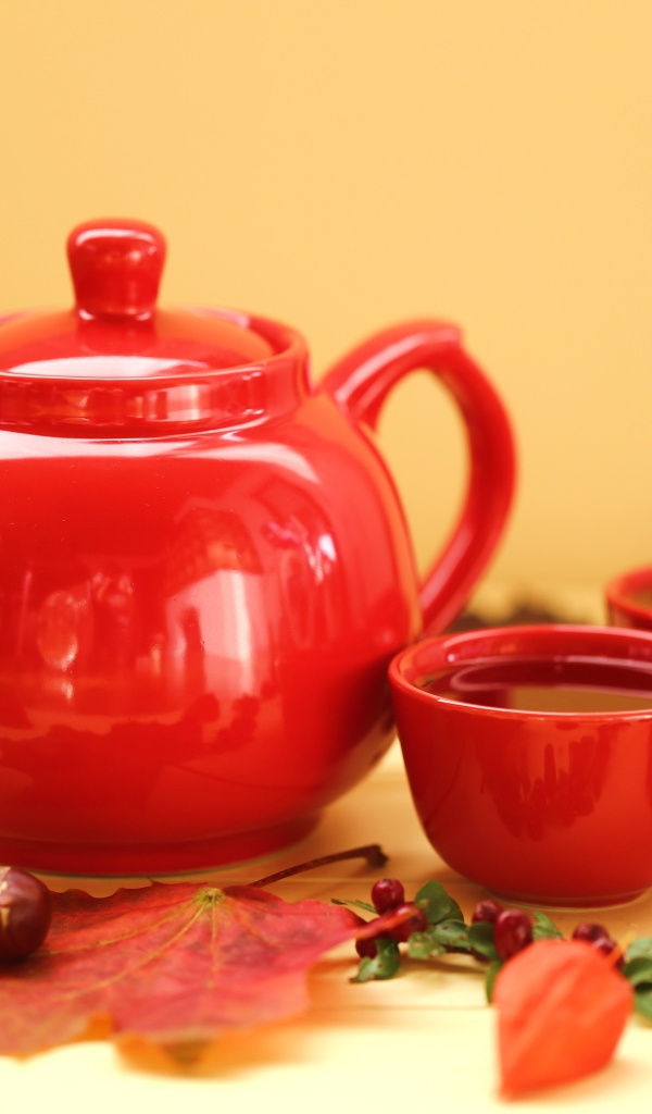 Красный чайник с чашками на столе осенью 