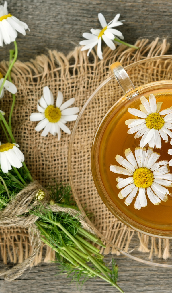 Чай в стеклянной чашке на столе с ромашкой