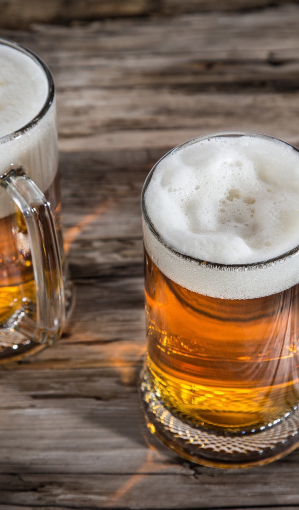 Два бокала пива с пеной на деревянном столе