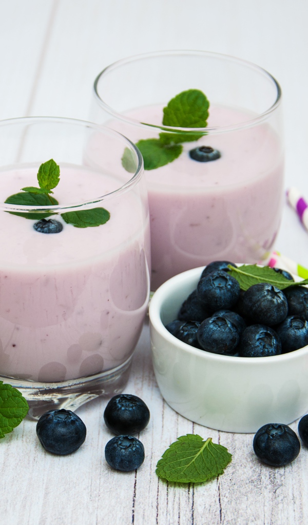 Два стакана коктейля в стаканах на столе с ягодами черники и трубочками