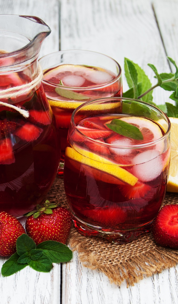 Два стакана мохито на столе с графином, лимоном, клубникой и мятой