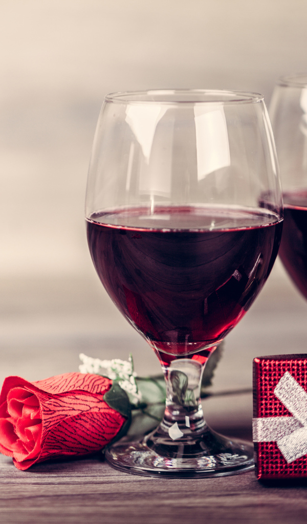 Два бокала вина на столе с подарками и красной розы 