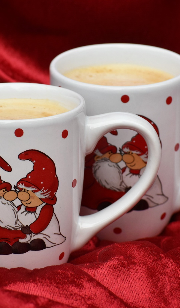 Две белые чашки кофе с рисунком стоят на красной ткани