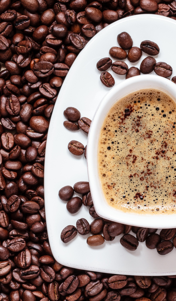 Белая чашка в форме сердца стоит на кофейных зернах 