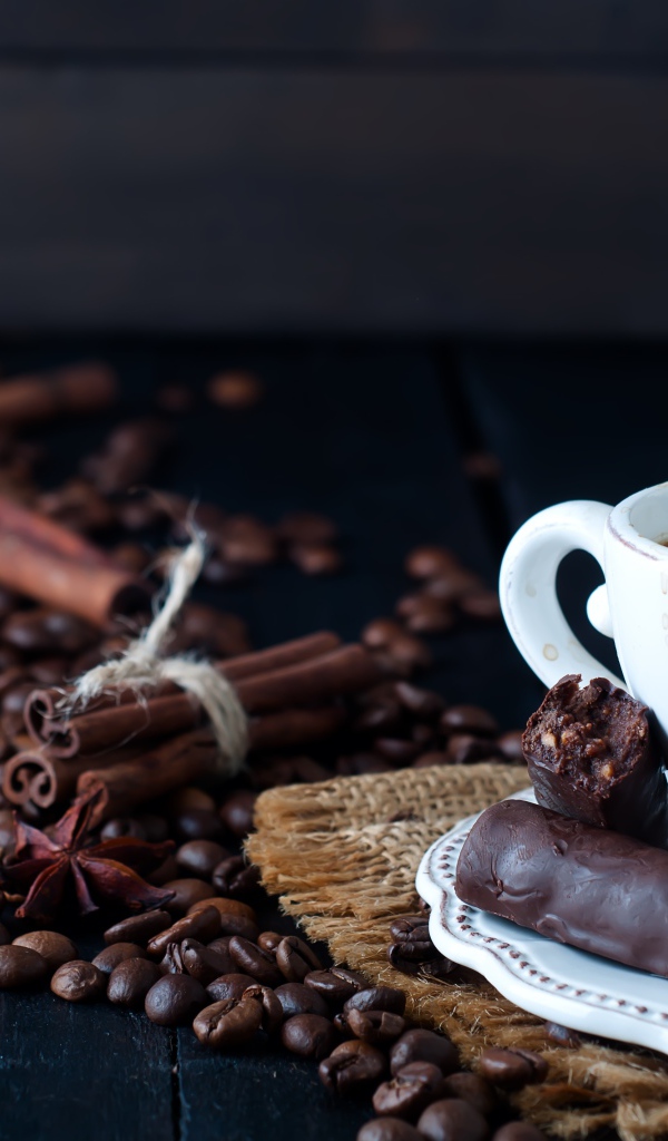 Белая чашка кофе на столе с конфетами, корицей, бадьяном и зернами