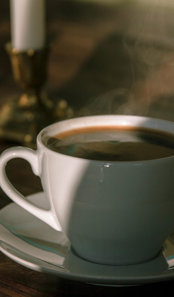 Белая чашка кофе на столе в лучах солнца