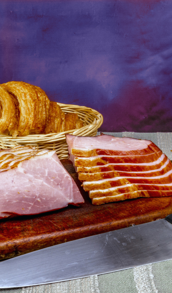 Кусок нарезанной ветчины на доске с круассаном
