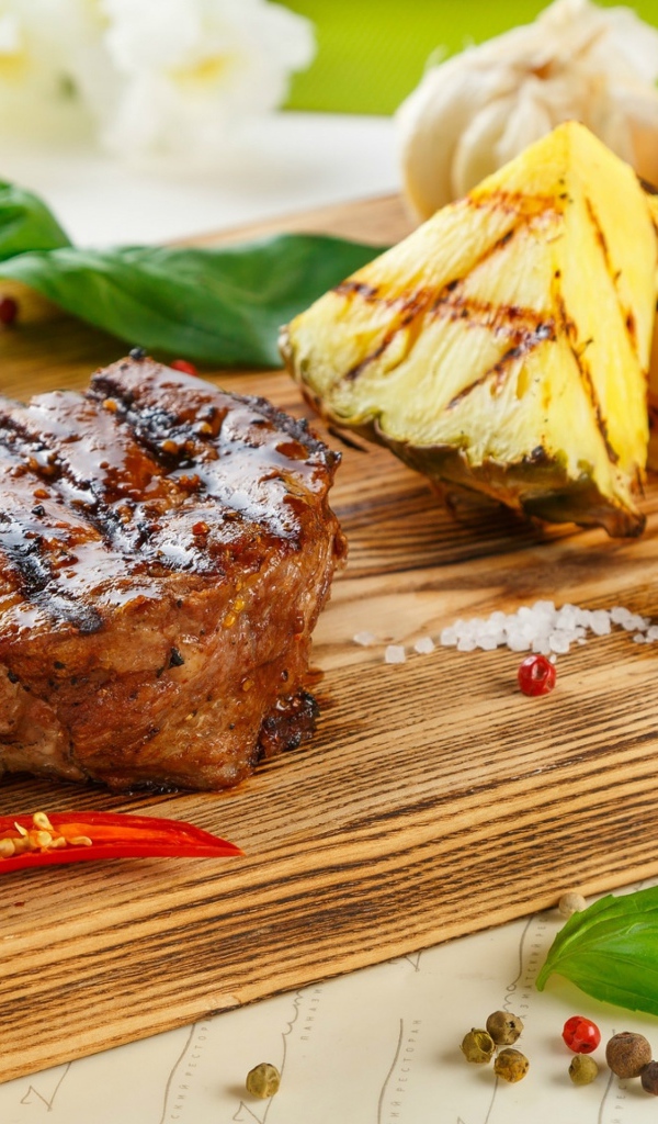 Кусок мяса гриль на деревянной доске с кусочками ананаса и базиликом