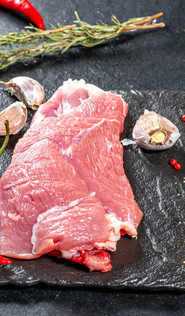 Кусок мяса на столе с острым перцем, чесноком и зеленью