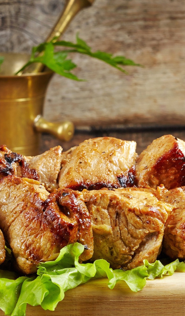 Аппетитный шашлык лежит на разделочной доске с листьями салата