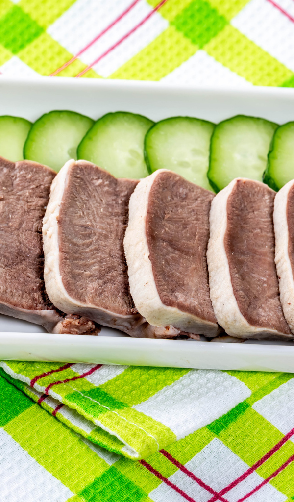 Вареный язык на тарелке со свежими огурцами