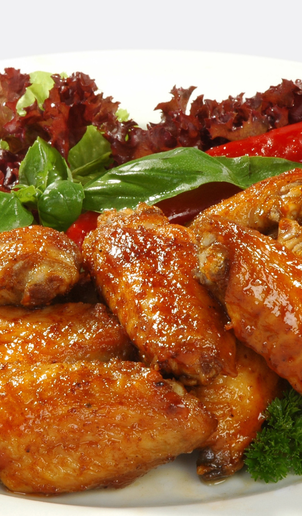 Жареные куриные крылышки на тарелке с острым перцем и зеленью 